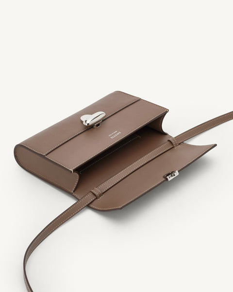 Brown leather handbag with a strap laid out flat and open on a white background