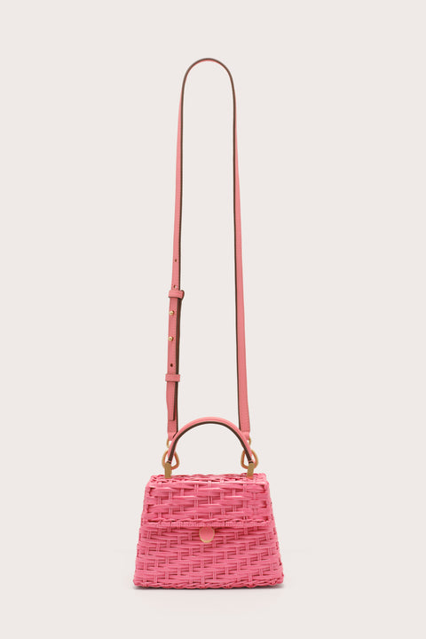 A pink wicker, trapezoidal handbag that features a top handle and flap closure, complete with gold-toned hardware and a detachable pink leather crossbody strap.