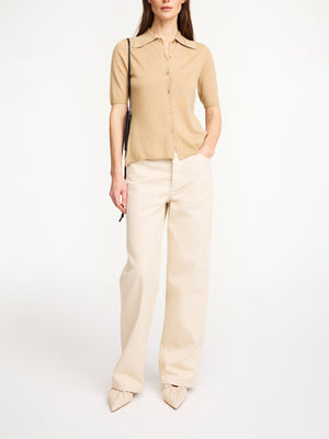 Woman wearing a beige blouse and cream wide leg denim on a white background