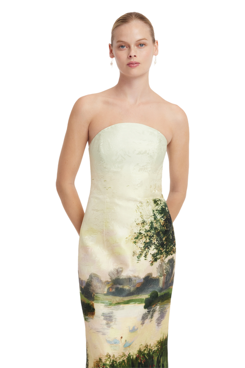 A woman modeling a strapless fitted dress with a cream lace bodice and a scenic landscape print on the skirt, shown against a plain white background.