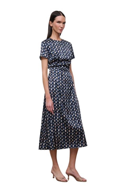 A woman modeling a short-sleeved midi dress with a navy blue base and a repeating beige and white floral pattern, paired with nude heeled sandals against a plain white background.