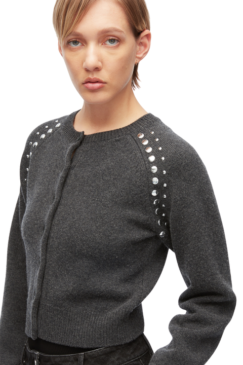 A woman wearing a dark gray knit cardigan with silver stud embellishments along the shoulders, shown against a plain white background.