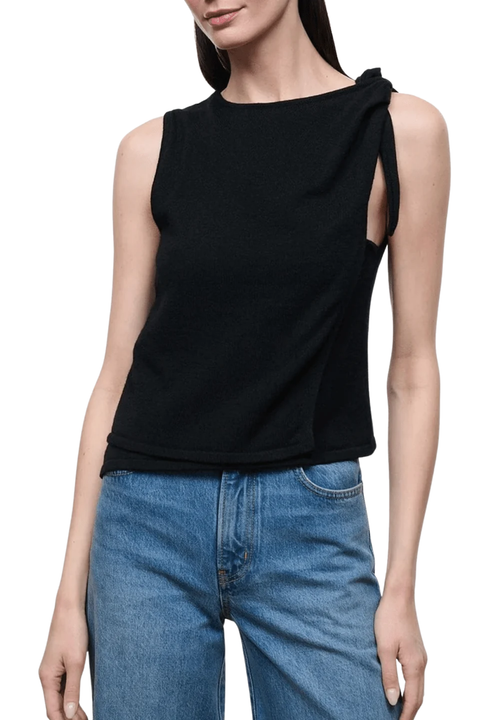 A woman wearing a black sleeveless knit top with side cutouts and tie details, paired with blue jeans, against a plain white background.