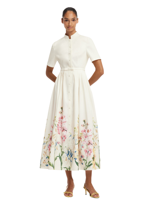 A woman modeling a white midi dress with short sleeves, a high collar, and a colorful floral print concentrated along the lower skirt, shown against a plain white background.