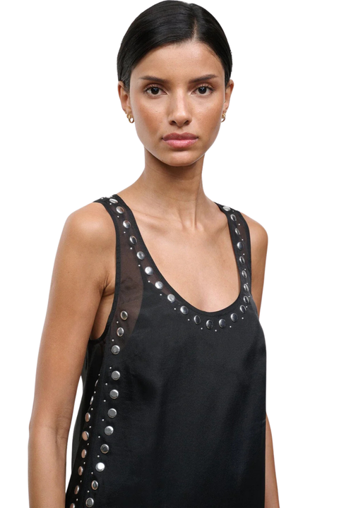 Woman wearing a black sleeveless mini dress with studs on a white background close up