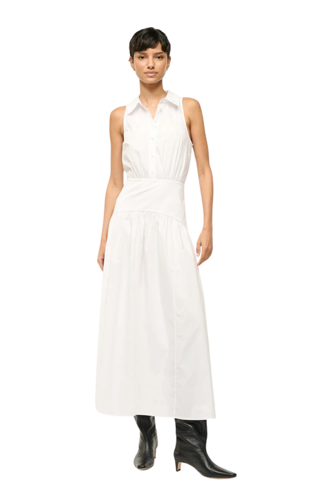 A model wearing a sleeveless white collared maxi dress with a gathered waist, paired with black pointed-toe heeled boots, shot against a solid white background.