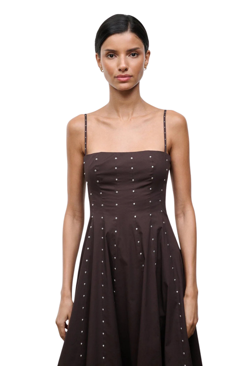 Woman wearing a long brown dress with silver studs on a white background close-up