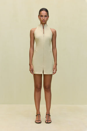 Woman wearing a khaki high-neck mini dress that features a utility design, front zipper, and sleek side pockets, paired with black sandals.