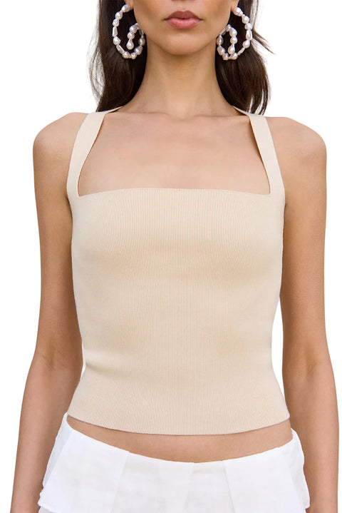 Detail shot of woman wearing a beige top and white pants holding a straw bag on a white background