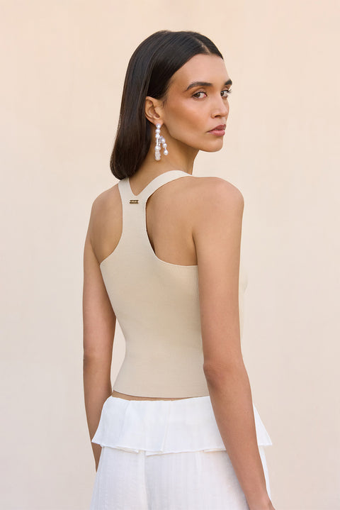 Back-facing shot of woman wearing a beige top and white pants holding a straw bag on a white background