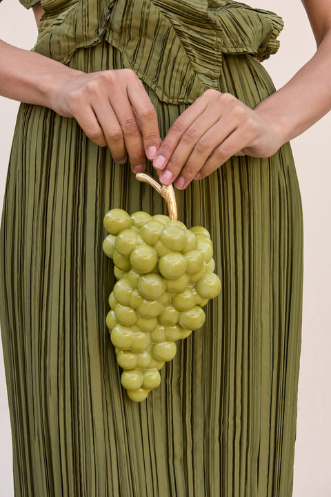 Woman holding a light green acrylic clutch that resembles a bunch of grapes with a gold toned stem.