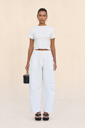 Woman wearing a pair of white, barrel-leg cargo pants, paired with a white top, black sandals, and black handbag,