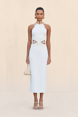 Woman wearing a white knit midi dress that features cutouts at the waist with a floral overlay and a floral applique at the neckline.