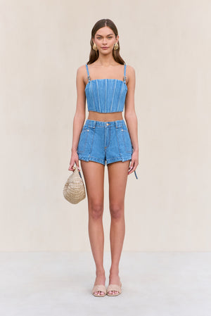 Woman wearing blue denim cargo shorts with a matching blue denim corset, paired with a woven handbag.