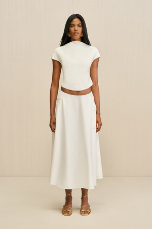 Woman wearing a white poplin, A-line midi skirt paired with a white top and gold sandals.