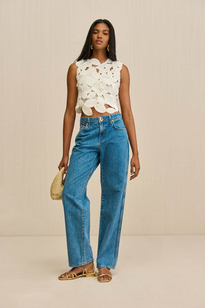 Woman wearing a white crochet tank top that is crafted from floral appliques sewn together, paired with blue jeans.