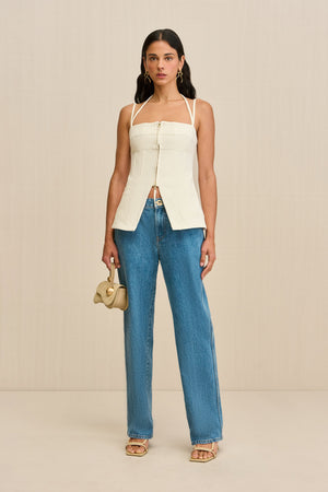 Woman wearing a white tank top that features a double strap detail, and front center zipper, and a flared cutout at the waist, paired with jeans and sandals.