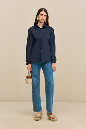 Woman wearing a navy button-down collared shirt, paired with blue jeans and tan sandals.