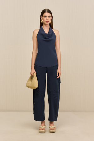 Woman wearing navy utility style barrel leg pants that hit at the ankle, paired with a blue top and tan sandals.