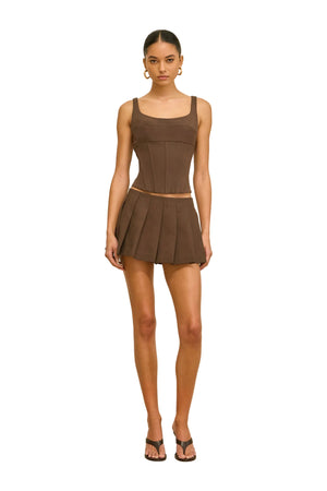 Woman wearing a brown sleeveless top and pleated mini skirt on a beige background.
