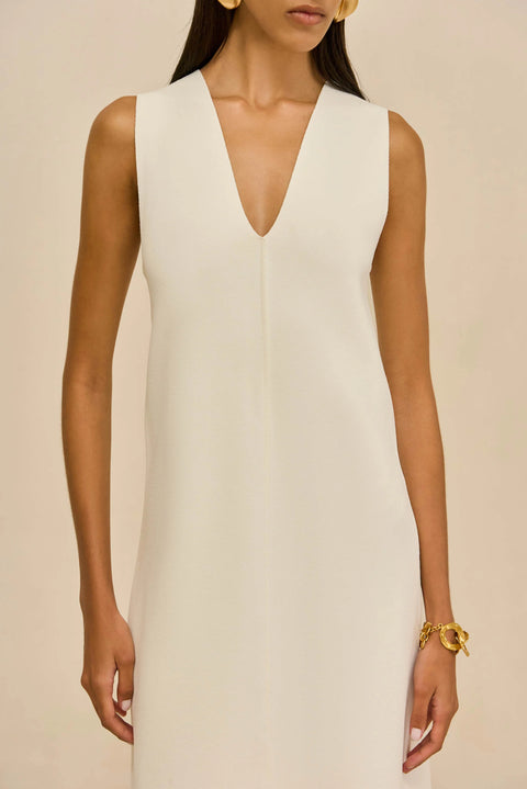 Zoomed in view of woman wearing a white sleeveless dress against a beige background