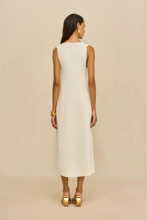 Back view of woman wearing a white sleeveless dress against a beige background.