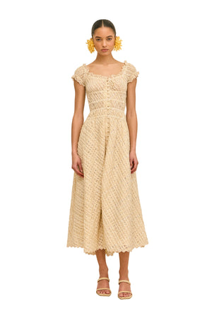 Woman wearing a woven beige dress with buttons against a beige background.