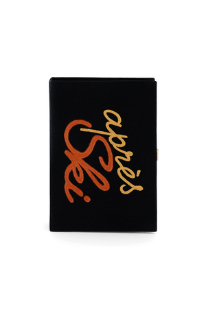 A black book clutch bag featuring a prominent embroidered design on the front. The design consists of a large orange and gold script reading "apres ski"