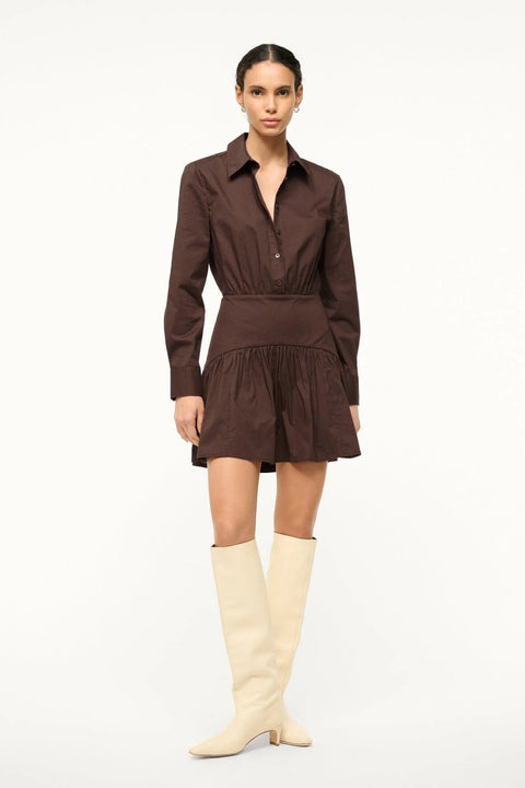 Woman wearing a brown poplin mini dress that features long sleeves and a curved yoke detail at the hip, paired with cream boots.