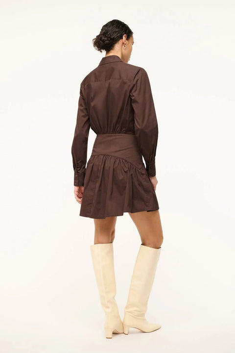 Back view of a woman wearing a brown poplin mini dress that features long sleeves and a curved yoke detail at the hip, paired with tall, cream boots.