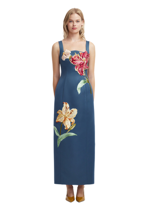 A woman modeling a sleeveless navy maxi dress with large floral prints in red, yellow, and green on the bodice and lower skirt, shown against a plain white background.