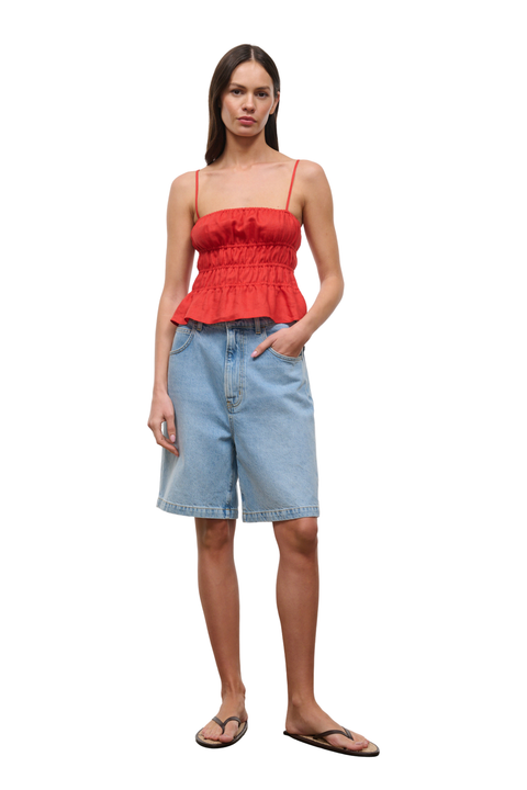A woman modeling a bright red peplum camisole top and light blue denim shorts against a plain white background.