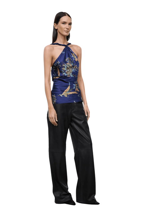 A model wearing a halter-neck top with a blue, gold, and white bird pattern, paired with black wide-leg pants, shown against a plain white background.