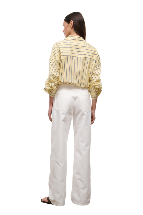 A woman shown from the back wearing a yellow and white vertically striped long-sleeve shirt and white wide-leg trousers, photographed against a plain white background.