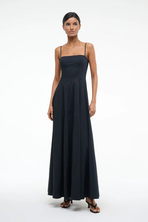 Woman wearing a black maxi dress that features spaghetti straps, a straight neckline, and corset style pleating, paired with black heels.
