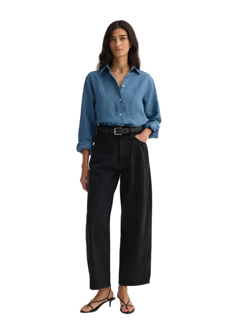 Woman wearing a blue denim shirt and black pants on a white background