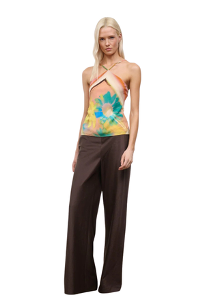 Woman wearing a colorful orange, yellow, and blue sleeveless halter neck top with brown linen pants