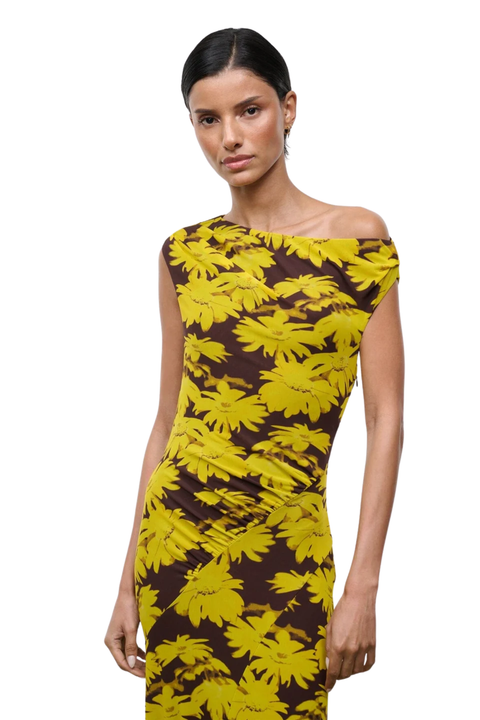 A woman modeling a fitted off-the-shoulder dress with a bold yellow floral print over a dark brown background, shot against a plain white studio backdrop.