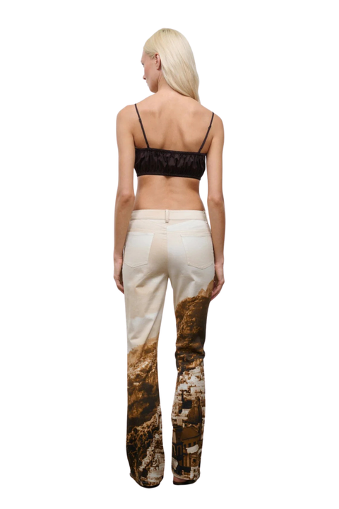 Woman wearing a brown top and cliffside patterned pants on a white background back angle