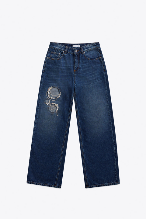 Front of dark wash blue jeans with a decorative crystal and chain cut outs on a white background