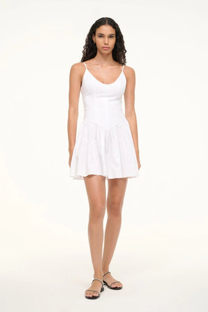 Woman wearing a white mini dress that features spaghetti straps and a scoop neck, a fitted bodice, and an A-line skirt, paired with sandals.