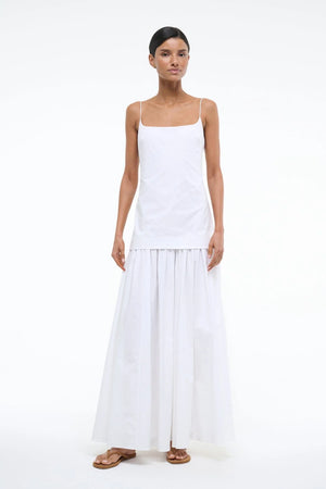 Woman wearing a sleeveless, white maxi dress that features a column fit drop waist with a gather poplin skirt.