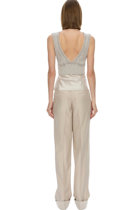 A model shown from the back wearing a light beige knit wrap-style top with a deep V-back and wide-leg satin trousers.