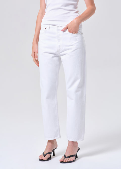 Person wearing a white sleeveless top and high-rise, straight leg, white jeans on a plain background with one hand in her pocket