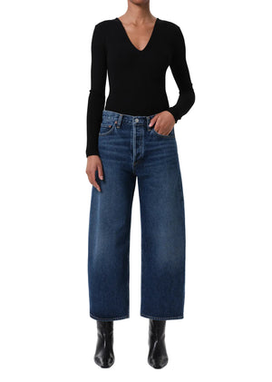 Person wearing a black long-sleeve top and blue wide-leg jeans on a white background