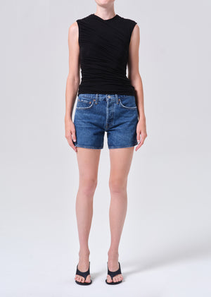 Person wearing a black sleeveless top and blue, high-rise denim shorts on a white background posing from the front