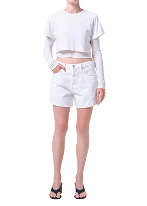 Person wearing a white long-sleeve crop top and white, high-rise denim shorts on a white background from the front