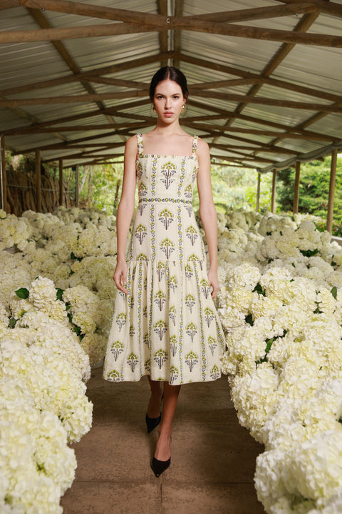 Model wears printed linen midi dress with square neck line on runway with white flowers.