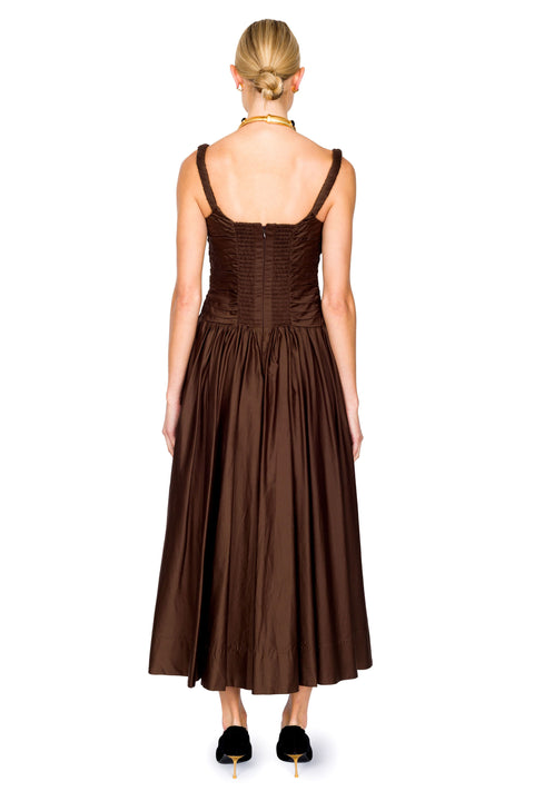 Woman facing the back wearing a brown dress with thin straps on a white background from the back