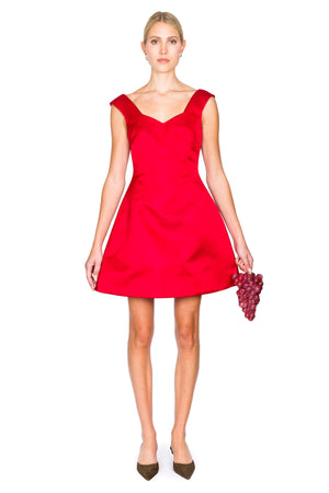Woman wearing a red mini dress with sweetheart neckline holding a grapes clutch on a white background